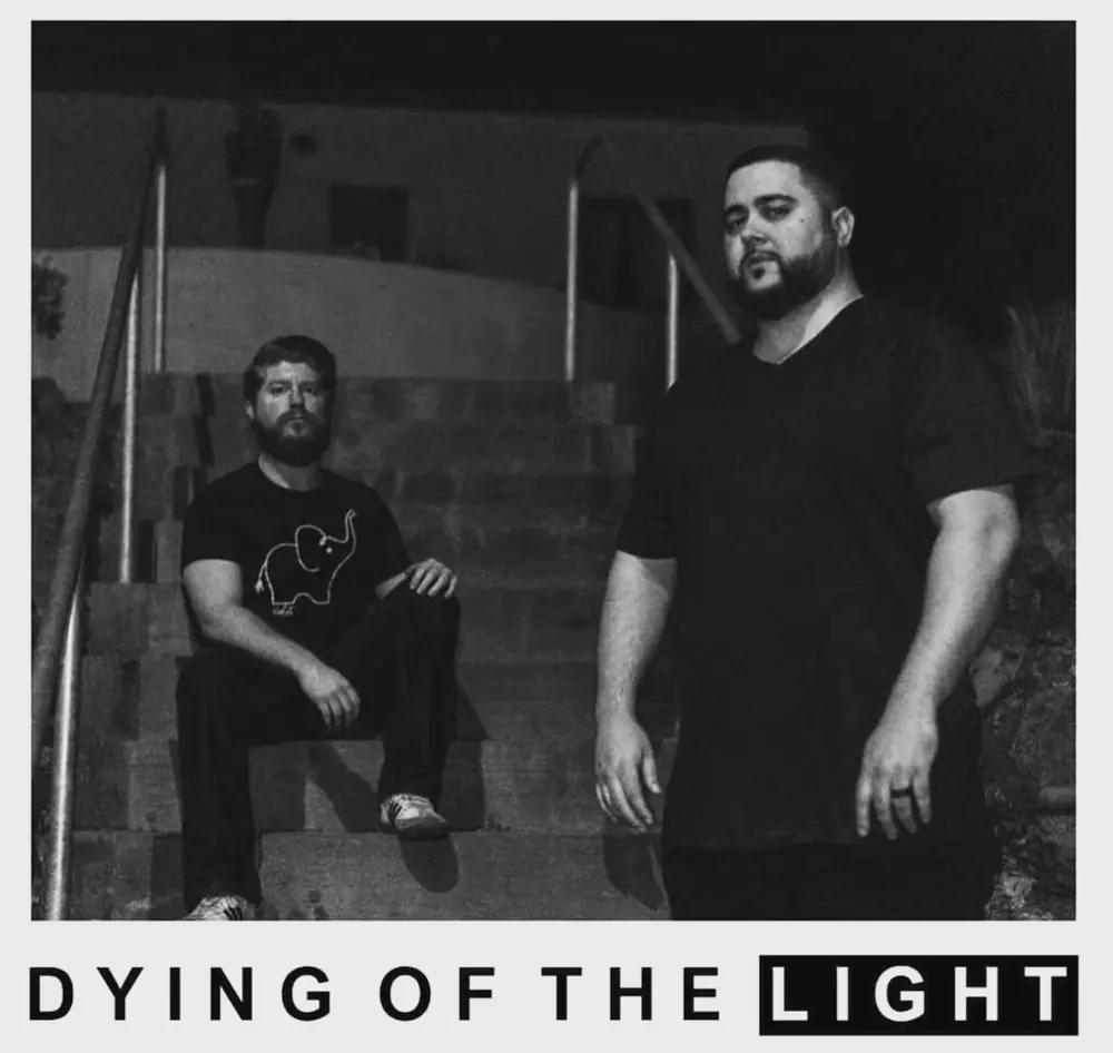 Black and white photo: Faulkner sitting on concrete steps at night, MC Solar Wind standing beside him, with the words Dying of the Light underneath