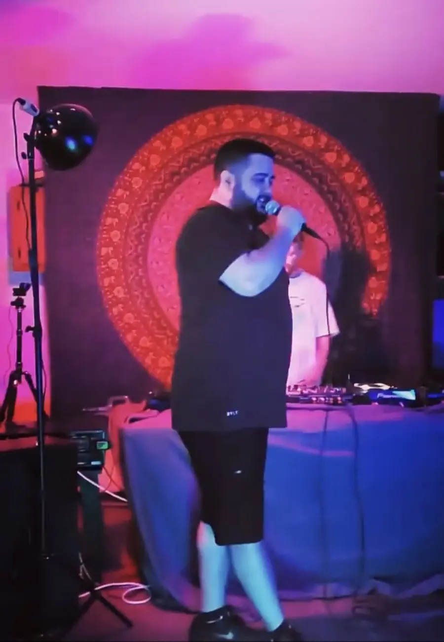 MC Solar Wind on the mic in front of a mandala backdrop, Faulkner on the decks behind him